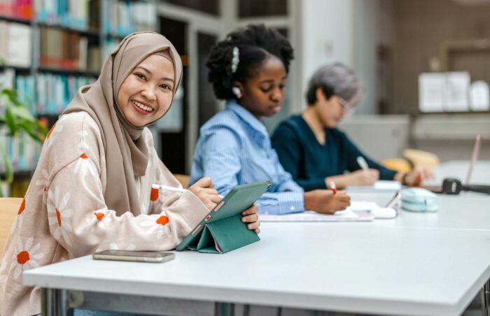 Woman in hijab sitting in the library studying with other students.